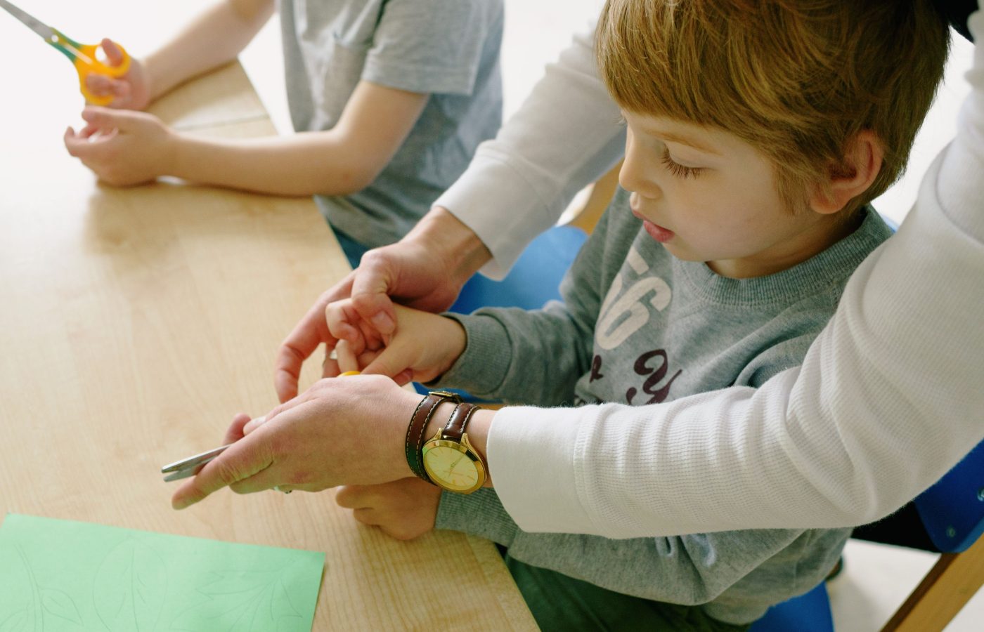 Kinder üben Feinmotorik mit der Schere unter Anleitung
